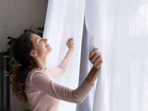 Happy young woman open curtains welcome new day.