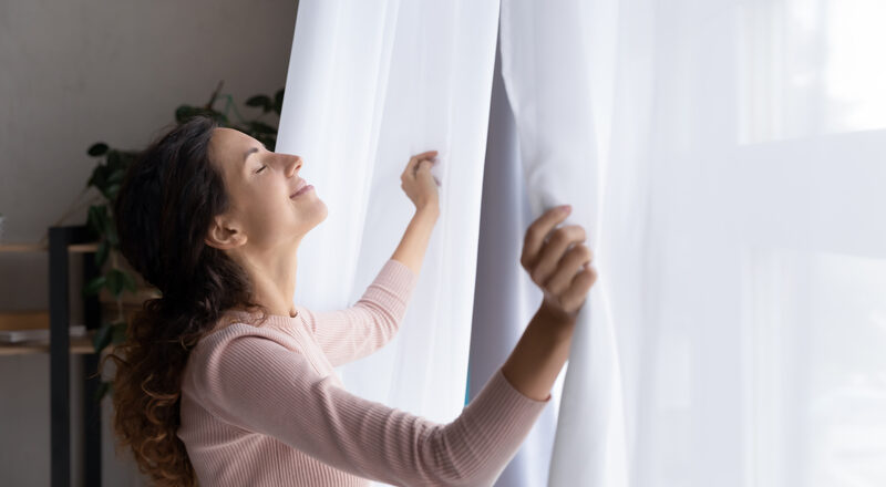 Happy young woman open curtains welcome new day.