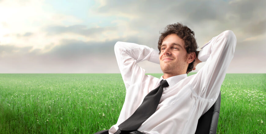 young businessman sitting on a chair on a green meadow